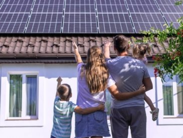 Eine Familie steht vor ihrem Haus mit einer frisch installierten Photovoltaik-Anlage auf dem Dach.