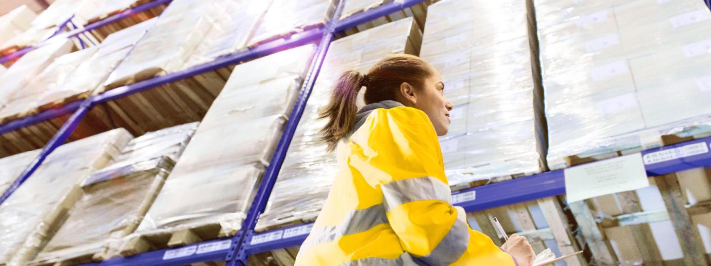 Logistikarbeiterin begutachtet die Waren in den hohen Regalen eines großen Lagers